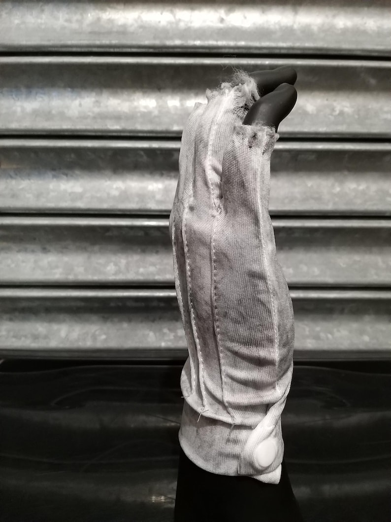 May include: A white cotton glove with a frayed edge and a button closure. The glove is worn and has a distressed look.