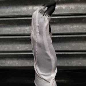May include: White cotton driving gloves with a button closure. The gloves are made of a thin, breathable fabric and have a ribbed texture.