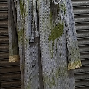 Puede incluir: Un camisón largo de rayas azules y verdes con ribete de encaje y cuello de ganchillo verde. El camisón tiene un lazo en el cuello y está manchado con manchas verdes.
