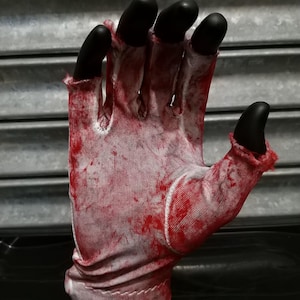 May include: A white glove with red blood splatter, the fingers are black and the glove is folded at the wrist.
