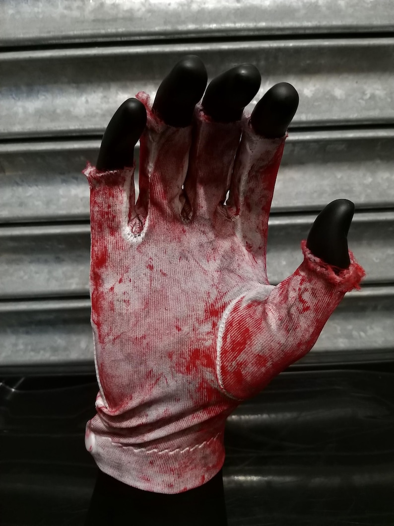 May include: A white glove with red blood splatter, the fingers are black and the glove is folded at the wrist.