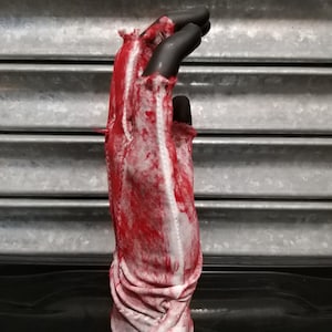 May include: A white glove with red splatters of paint, appearing as blood, on the fabric. The glove is ripped and torn, giving it a distressed look.