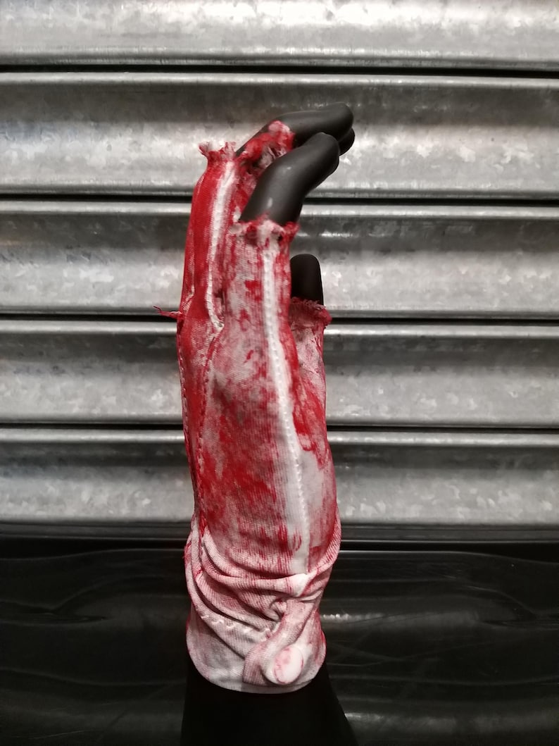 May include: A white glove with red splatters of paint, appearing as blood, on the fabric. The glove is ripped and torn, giving it a distressed look.