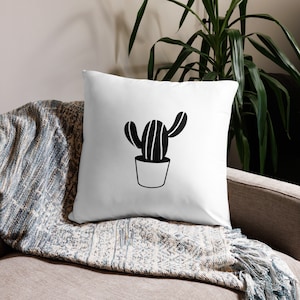 May include: White cushion with a black silhouette of a potted cactus. The cactus has a striped pattern and is in a simple pot.