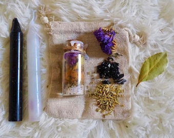 Könnte beinhalten: Eine kleine Glasflasche gefüllt mit getrockneten Kräutern, Blumen und Kristallen. Die Flasche ist umgeben von anderen Zutaten, darunter ein Lorbeerblatt, schwarze Kristalle und getrockneter Rosmarin. Es gibt auch zwei Kerzen, eine schwarze und eine weiße.