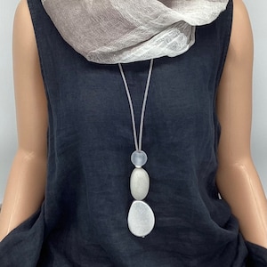 May include: A grey and white scarf is draped around the neck of a mannequin wearing a black sleeveless dress. A long necklace with three grey and white stone beads hangs from the neck.