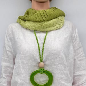 以下が含まれることがあります： 緑色のガラス製の円形のペンダントネックレス。木製のビーズと緑色の紐が付いています。