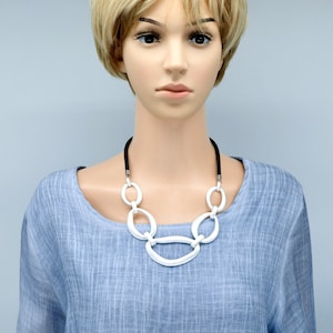 May include: A mannequin wearing a light blue, textured blouse with a silver chain necklace. The necklace has large, oval-shaped links.