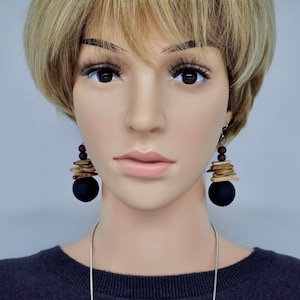 May include: A mannequin wearing a black sweater and a silver necklace with black and wood earrings. The earrings feature a large black bead and stacked wood pieces.