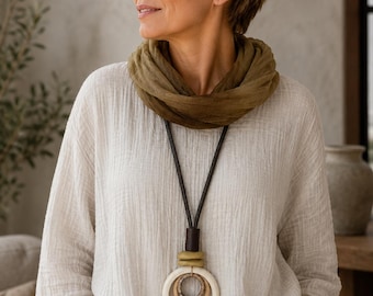 May include: A long necklace featuring a dark brown leather cord with a large pendant composed of a smooth white ring, a smaller textured brown ring, and a small olive green ring, all suspended from a dark brown cylindrical bead connector.