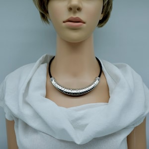 May include: A silver choker necklace with a textured, curved design. The necklace is on a white mannequin.