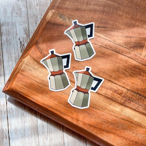 Könnte beinhalten: Drei braune und grüne Kaffeekannen-Aufkleber auf einer Holzoberfläche.