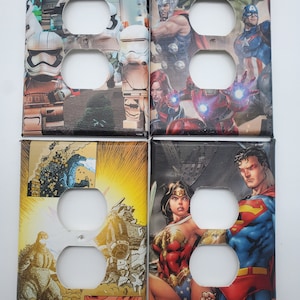 May include: Four decorative outlet covers featuring comic book characters. The top left cover features Star Wars characters, the top right cover features Marvel characters, the bottom left cover features Godzilla, and the bottom right cover features Wonder Woman and Superman.