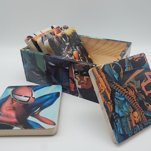 May include: Wooden box and coasters featuring comic book characters. The box is decorated with images of Batman and other heroes. The coasters display Spider-Man and Spawn. The box is open, revealing more coasters inside.