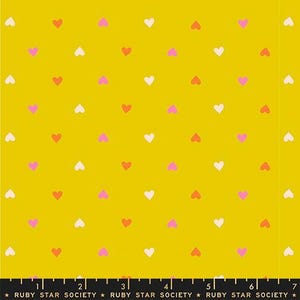 May include: Mustard yellow fabric with a repeating pattern of small hearts in white, pink, and coral. The fabric has a ruler along the bottom with the text "RUBY STAR SOCIETY".