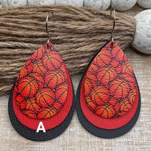 May include: A pair of layered teardrop earrings with a basketball pattern. The earrings are red, orange, and black. The earrings have a silver hook.