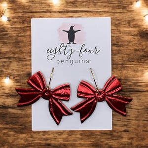 May include: Red bow earrings with gold hoops. The earrings are on a white card with the text "eighty-four penguins".