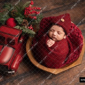 Peut inclure: Un nouveau-né emmailloté dans une couverture en tricot rouge et un bonnet en tricot rouge. Le bébé est couché dans un bol en bois avec une couverture en tricot rouge. Le bébé dort paisiblement.