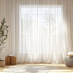 Könnte beinhalten: Heller Innenraum mit einem großen Fenster, das von transparenten weißen Vorhängen umrahmt wird. Eine Topfpflanze, zwei Holzstühle mit einem Buch und ein geflochtener Hocker mit einem Kissen befinden sich im Raum. Sonnenlicht scheint durch das Fenster.