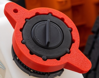 Op de afbeelding: Een rode en zwarte plastic dop met de tekst "ROTO-PAX.com" erop. De dop heeft een kleine zwarte hendel aan de bovenkant.