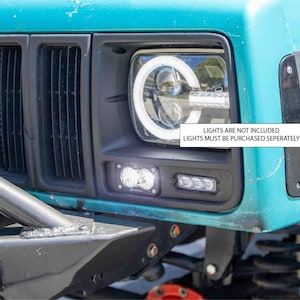 May include: A teal Jeep with a black front bumper and grill. The headlights are aftermarket and have a halo ring. The text on the bumper reads "LIGHTS ARE NOT INCLUDED LIGHTS MUST BE PURCHASED SEPARATELY".