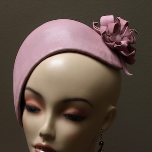 Puede incluir: Un maniquí con un sombrero de cuero rosa con un adorno floral, un collar de cuentas azul oscuro y verde, y pendientes colgantes con una piedra roja oscura.