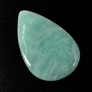 May include: A teardrop shaped light blue aquamarine gemstone with white streaks and a polished finish.