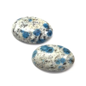 May include: Two oval-shaped blue and white polished stones. The stones have a speckled pattern with blue flecks on a white background.