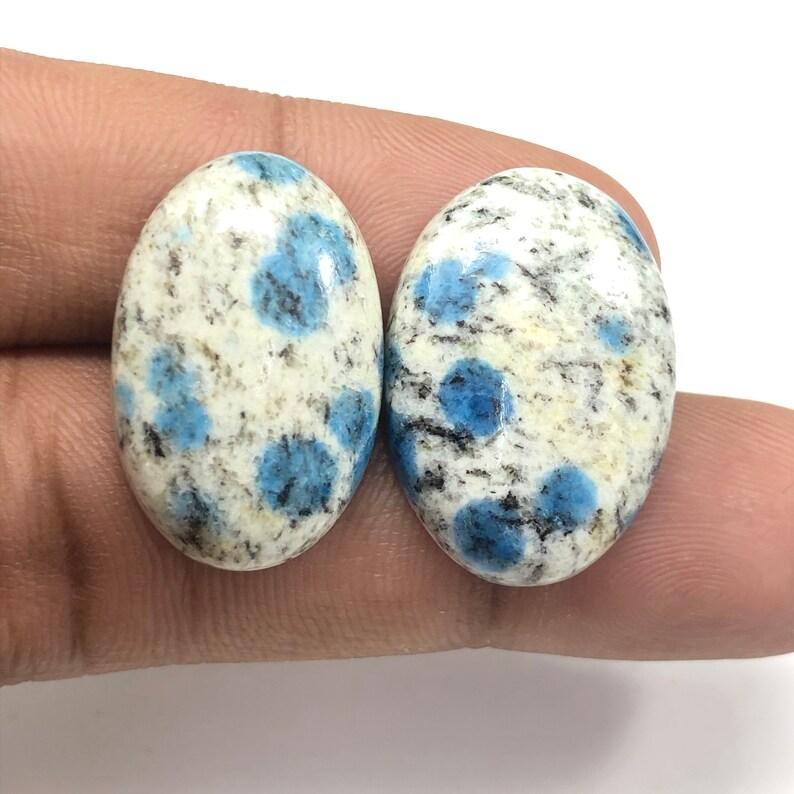 May include: Two oval-shaped blue and white speckled cabochons. The cabochons are a light blue color with white and black speckles.