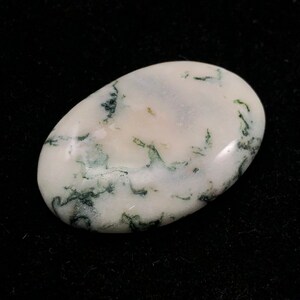 Pode incluir: Um caboch&atilde;o de &aacute;gata musgosa branco e verde, polido e de forma oval. A pedra tem uma base branca com inclus&otilde;es verdes que se assemelham a musgo.