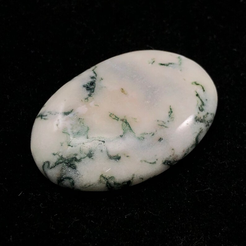 Pode incluir: Um caboch&atilde;o de &aacute;gata musgosa branco e verde, polido e de forma oval. A pedra tem uma base branca com inclus&otilde;es verdes que se assemelham a musgo.