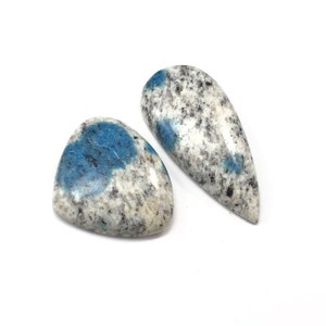 May include: Two K2 Azurite stones. One is triangular, the other is teardrop-shaped. Both stones have a white and gray speckled pattern with patches of blue. The stones are set against a white background.