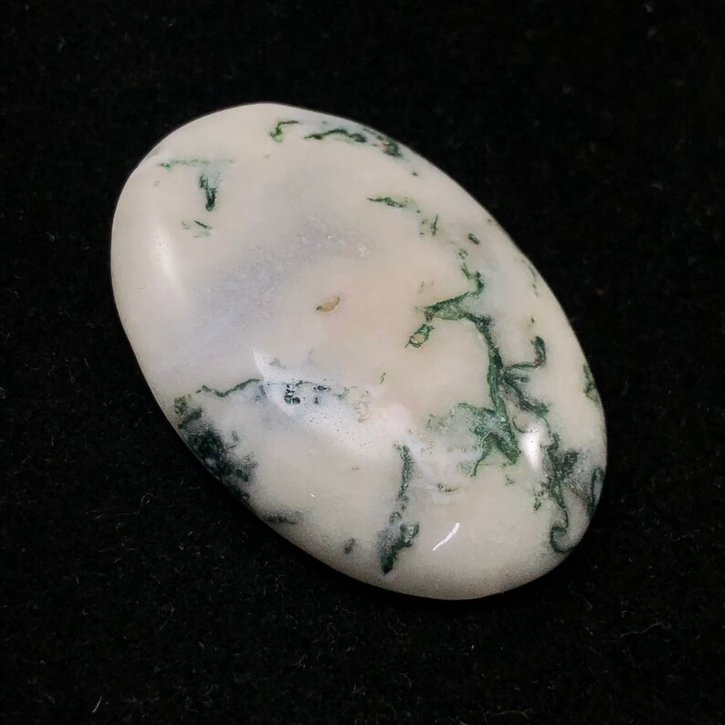 Pode incluir: Um caboch&atilde;o oval branco com inclus&otilde;es de &aacute;gata verde musgo. A pedra tem uma superf&iacute;cie lisa e polida.