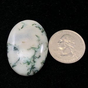 Pode incluir: Um caboch&atilde;o de &aacute;gata branco e verde com um padr&atilde;o de redemoinho. O caboch&atilde;o &eacute; aproximadamente do tamanho de uma moeda de 25 centavos de d&oacute;lar americano.