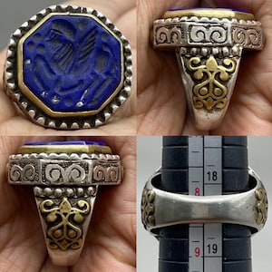 Könnte beinhalten: Ein Silberring mit einem großen, achteckigen, tiefblauen Stein. Der Stein ist in einer goldenen Lünette gefasst und weist ein geschnitztes Design auf. Der Ring hat verzierte Silber- und Golddetails am Band.
