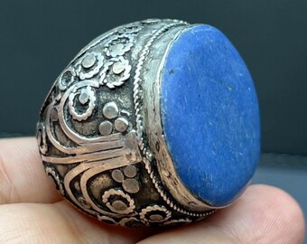 May include: A silver ring with an oval, deep blue stone. The ring's band features intricate, ornate patterns and designs. The stone is set in a bezel setting, and the ring appears to be vintage or antique.