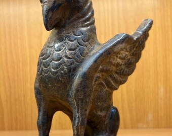 May include: A dark bronze griffin statue with detailed feather and wing textures. The mythical creature is seated, with its wings spread slightly. The statue has a bird-like head and a strong, muscular body, showcasing a blend of avian and feline features.