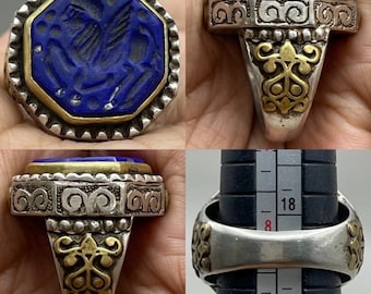 Può includere: Un anello d'argento con una pietra di lapislazzuli blu, con un disegno inciso. La pietra è incastonata in una lunetta d'oro e l'anello presenta dettagli ornati in argento e oro. L'anello è mostrato da più angolazioni.