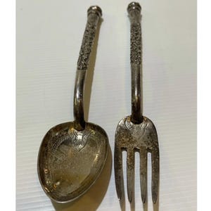 May include: A silver spoon and fork set. The spoon has a rounded bowl and the fork has three tines. Both utensils have ornate, textured handles and are likely vintage or antique.