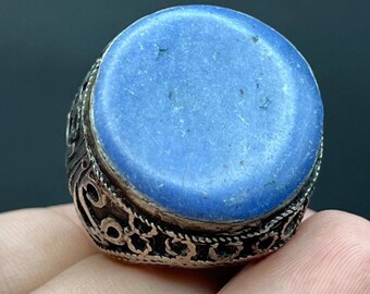 May include: A silver ring with a large, oval, light blue stone. The ring's band features intricate, openwork designs. The stone has a slightly uneven surface, and the ring appears to be vintage or antique.