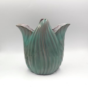 Pode incluir: Um vaso de cerâmica com um design semelhante a uma tulipa. O vaso tem um acabamento brilhante com tons de verde-azulado e castanho, e um interior lilás claro. O vaso tem uma forma única e orgânica e é adequado para decoração de casa.