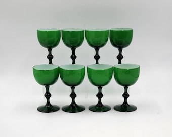 May include: Eight green stemmed glasses with black stems and bases are arranged in two rows. The glasses have a rounded bowl shape and a contrasting white interior. The glasses are likely for serving beverages.