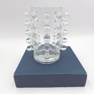 May include: A clear glass vase featuring a cylindrical body adorned with vertical rows of raised, spherical glass studs. The vase has a smooth, open top rim and a flat base, showcasing a transparent design that catches light through its textured surface.