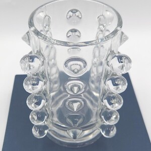 May include: A clear glass cylindrical vase featuring a textured surface with multiple protruding spherical glass bubbles arranged in vertical rows around the exterior. The glass is transparent and smooth, with a wide circular opening at the top.