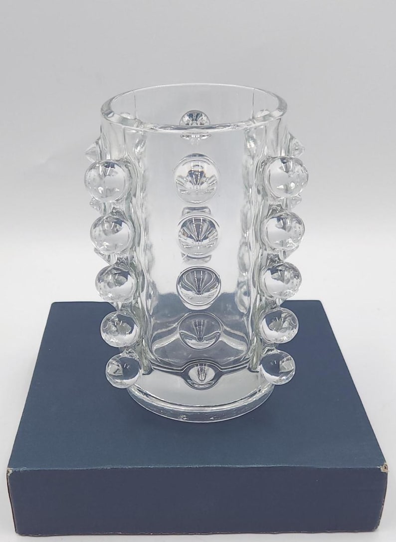 May include: A clear glass cylindrical vase featuring a repeating pattern of raised, spherical glass bubbles arranged in vertical columns around the exterior surface. The vase has a smooth, open top rim and a flat base, showcasing a transparent design.