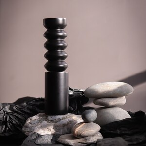 May include: A black ceramic vase with a textured, segmented design sits on a gray rock. The vase is surrounded by gray rocks and black crumpled paper.