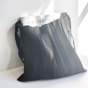 May include: A black pleated tote bag with a white book inside. The book has the text "THE KINFOLK" on the cover.