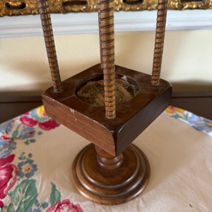 May include: A wooden stand with four spindles and a circular top. The stand has a square base and a round pedestal.