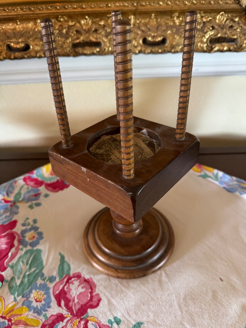 May include: A wooden stand with four spindles and a circular top. The stand has a square base and a round pedestal.