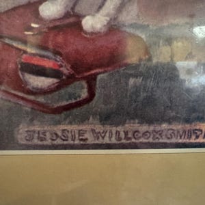 May include: Framed artwork featuring a watercolor painting with a red object and the artist's signature, "JESSIE WILLCOX SMITH." The artwork is set against a muted background, with a tan mat and a gold-toned frame.